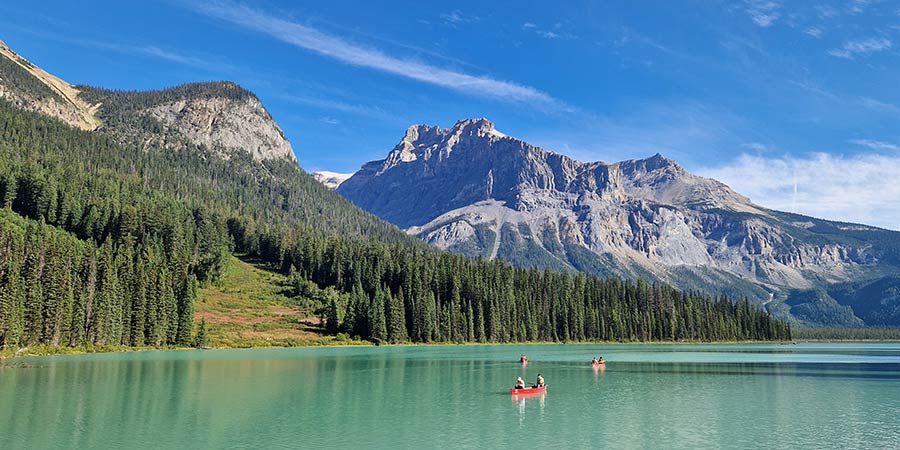 Three red canoes ride along the crystal-clear water of Lake Louise, with green trees and vast mountains behind them. 